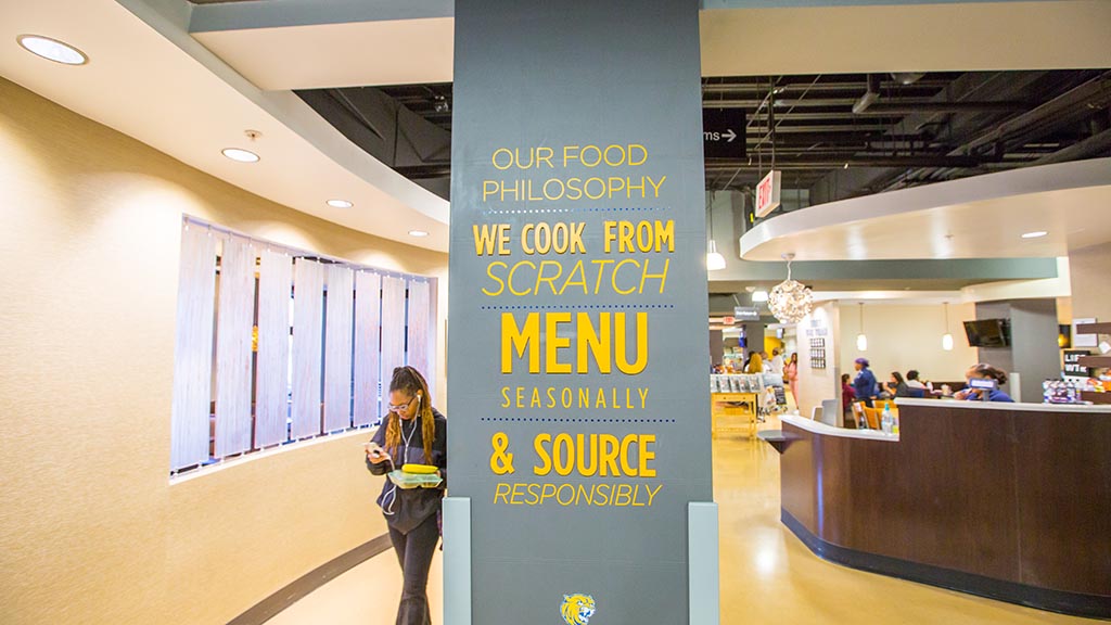 a student exiting JWU Charlotte's dining hall passes a sign promoting fresh and local ingredients