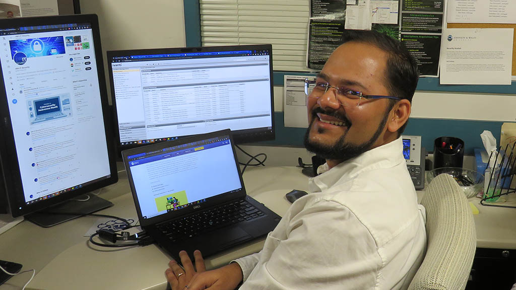 a photo of Vishal Ojha pausing to smile for the camera while working on a computer