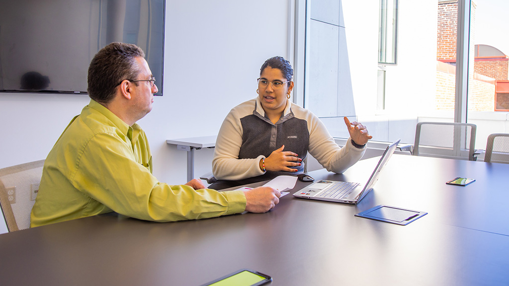 A student and a professor sitting at a table with a laptop