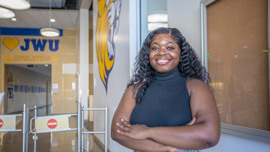 a photo of Vanessa Beke ’23 posing with a smile and crossed arms in the lobby of JWU's Wildcat Center