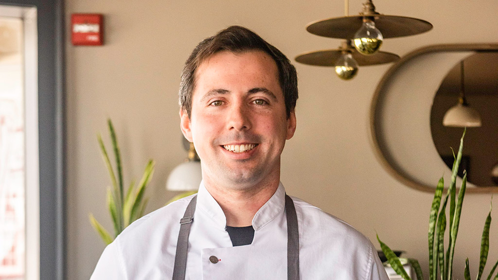 photo of Luke Mersfelder '16 pausing and smiling at the restaurant where he works as chef de cuisine