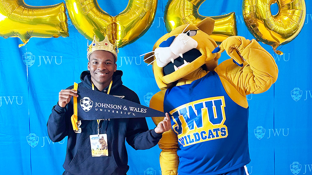 A student wearing a crown posing with Wildcat Willie