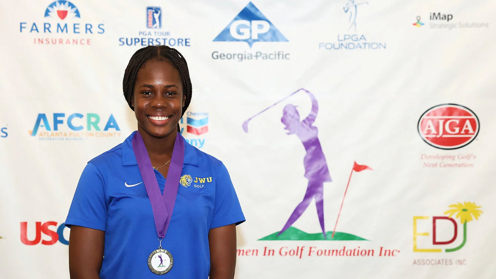 Hopal Richards '24 poses with her USCAA Female Golf Student-Athlete of the Year medal in front of a backdrop of sponsor logos