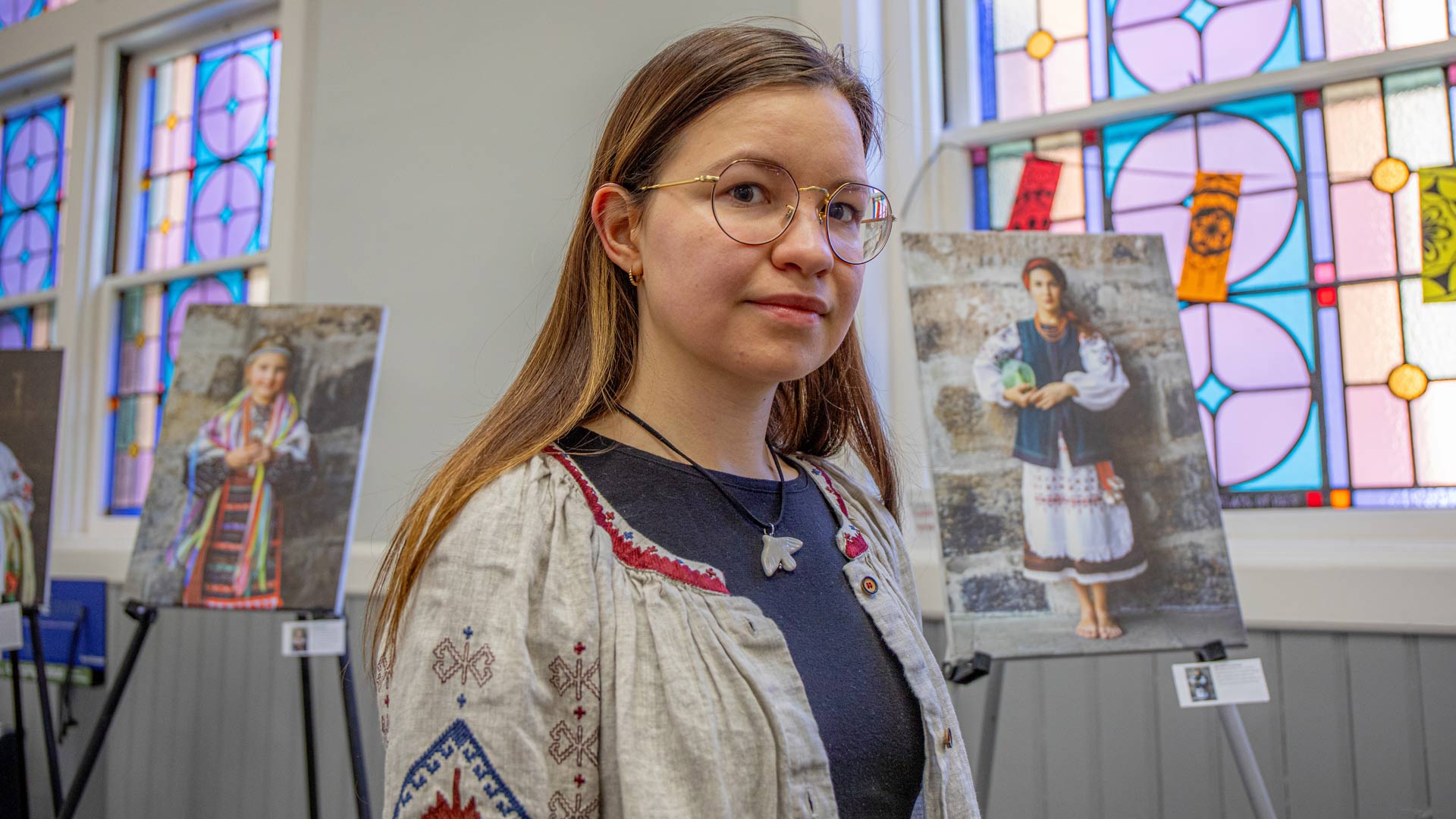 a woman dressed in traditional Ukrainian clothing stands before an art exhibit