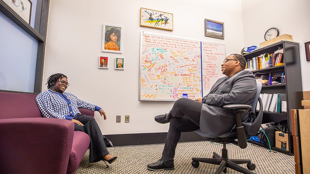 Student sits on a couch and talks with an advisor seated in a chair