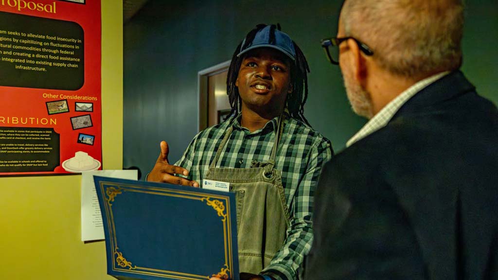 Tymon childs presenting his project, Feed the Folk: Soybeans as SNAP Inputs, and holding the award he won.