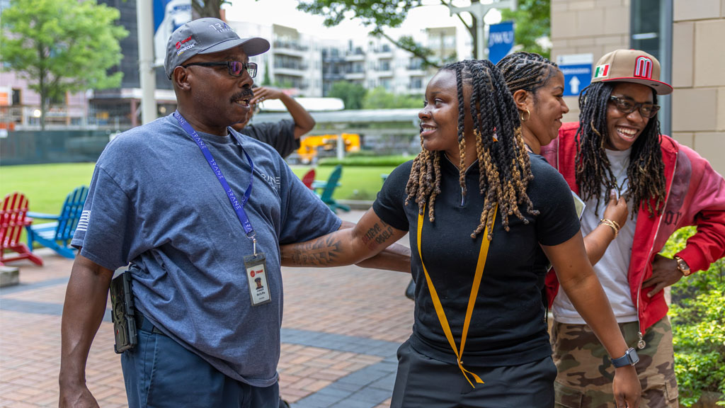Two people smiling at each other, with people laughing in the background.