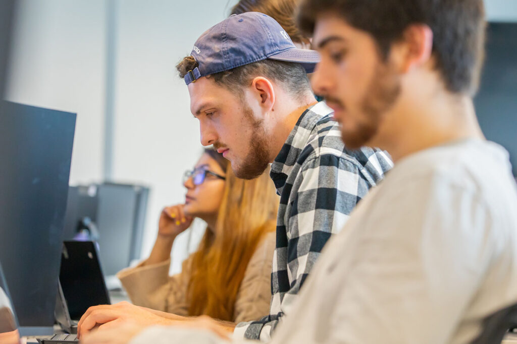 Students seated at computers in a classroom, focused on their screens.