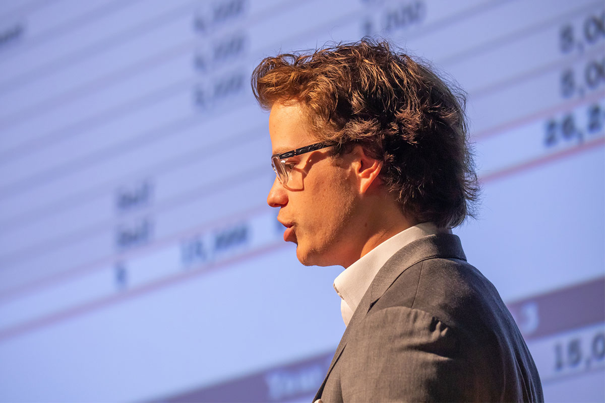 A student gives a presentation before a large screen displaying financial data.