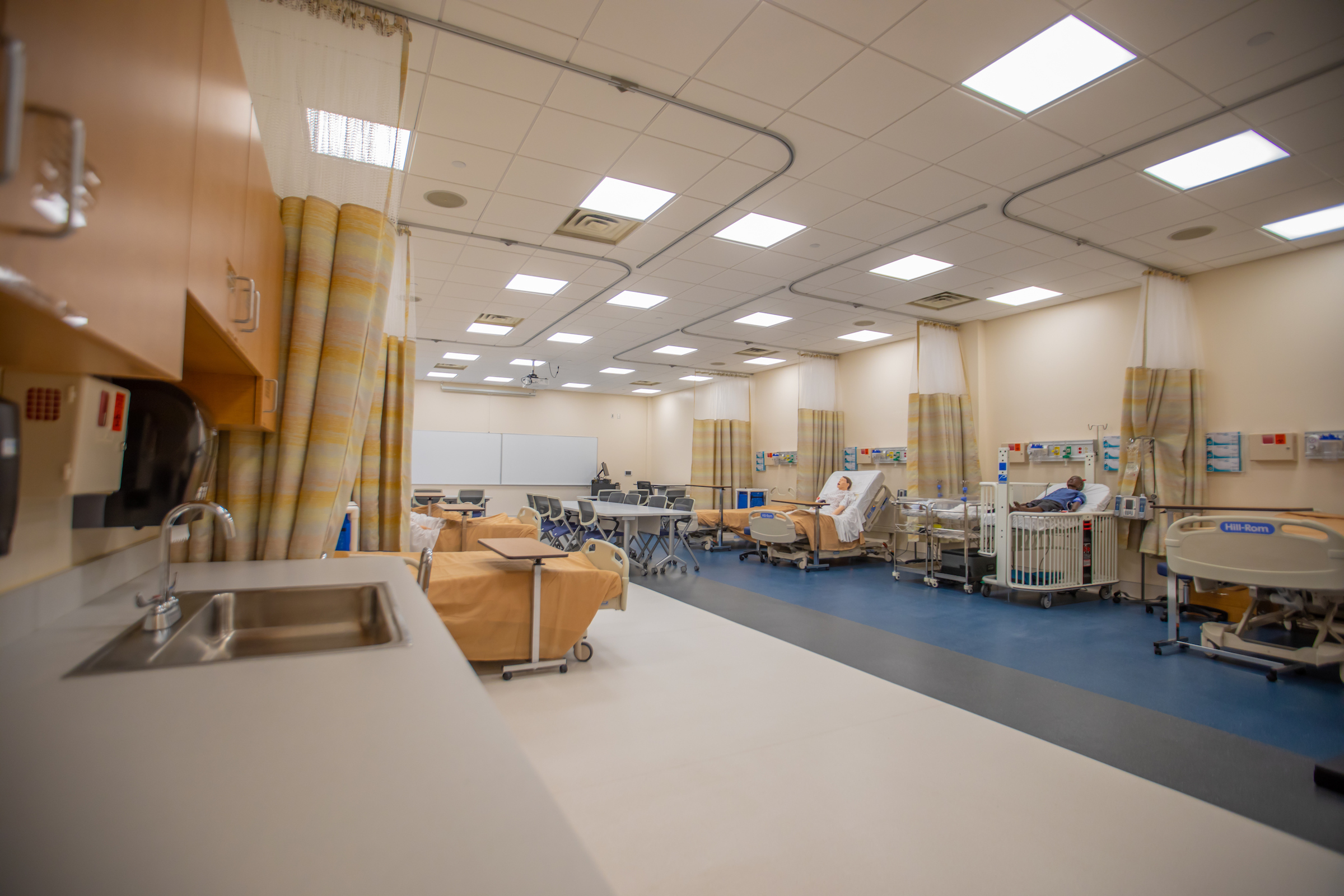 A hospital simulation room with beds, medical equipment, and a sink in the foreground.