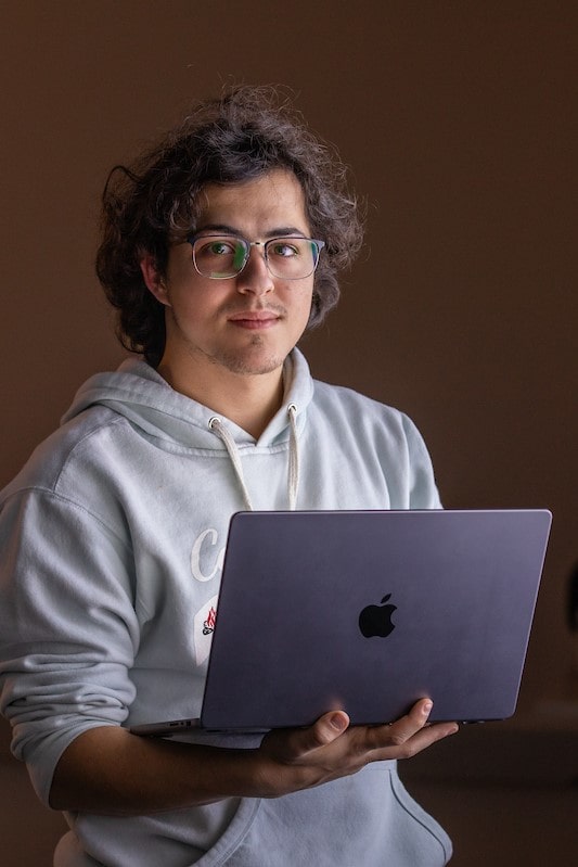 male student in grey sweatshirt holding macbook