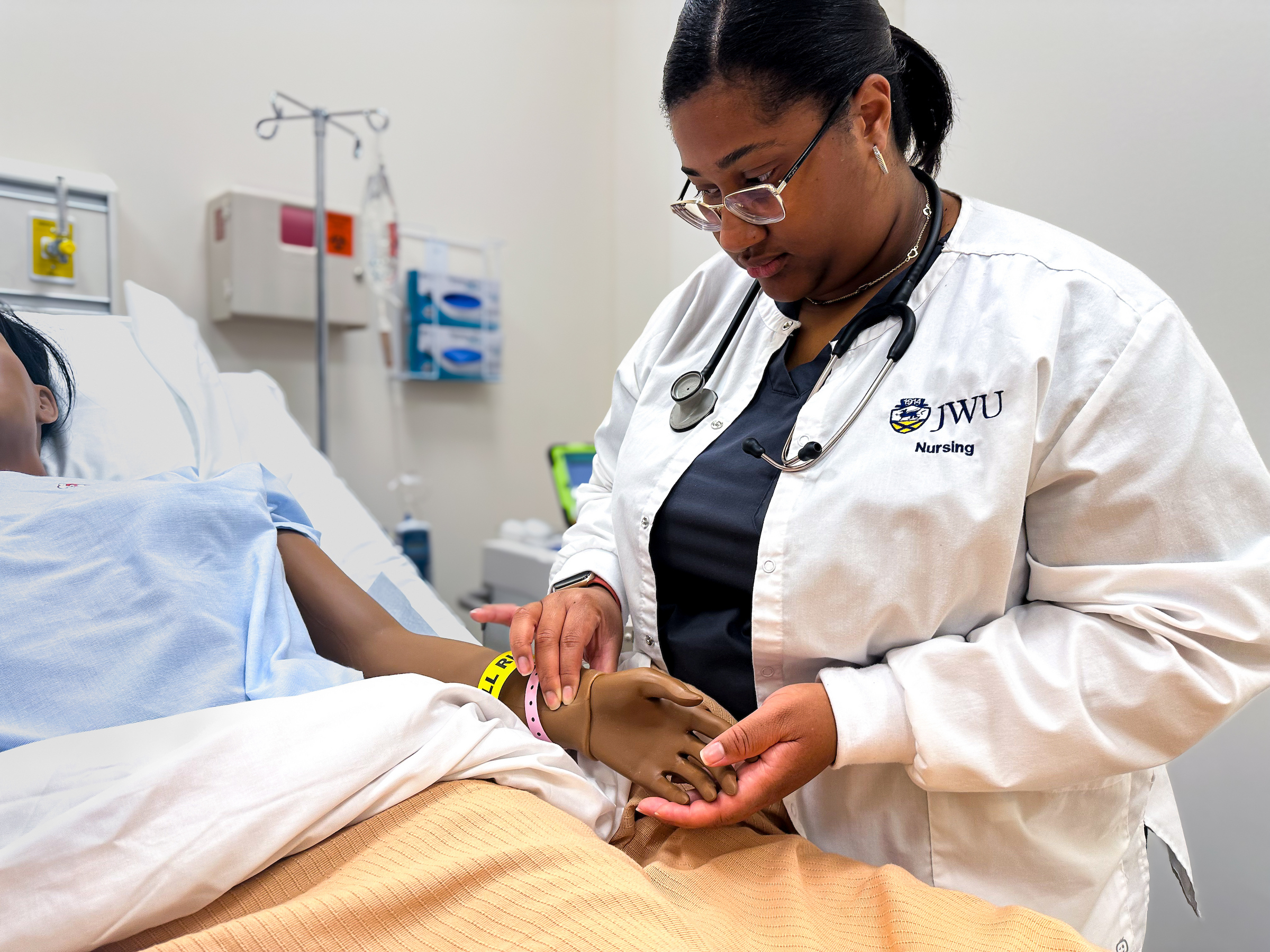 A healthcare professional in a white coat with a stethoscope attends to a patient lying in a hospital bed, performing a hands-on examination.