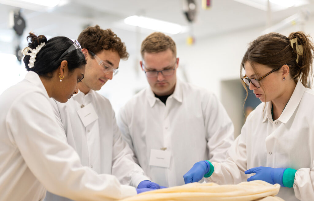 A group of people in white lab coats standing around a table inside a lab.