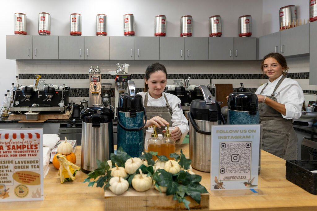 Two individuals in aprons prepare beverages at a counter adorned with autumn-themed decorations and promotional signs.