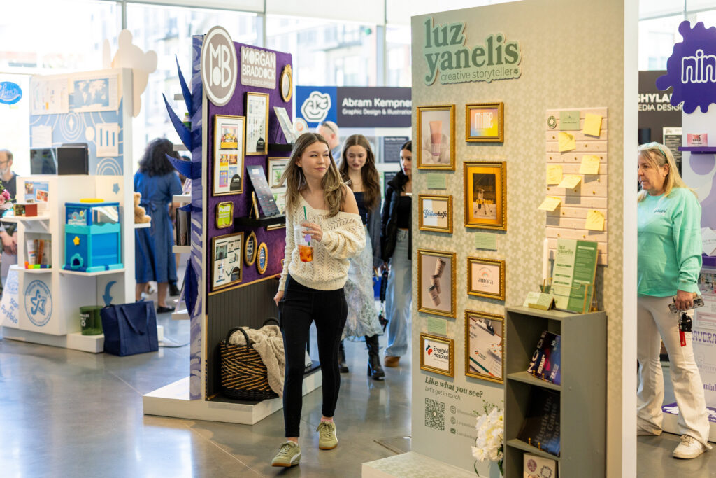 A person walks through an indoor exhibition space, passing by colorful display booths featuring branding and creative design work.