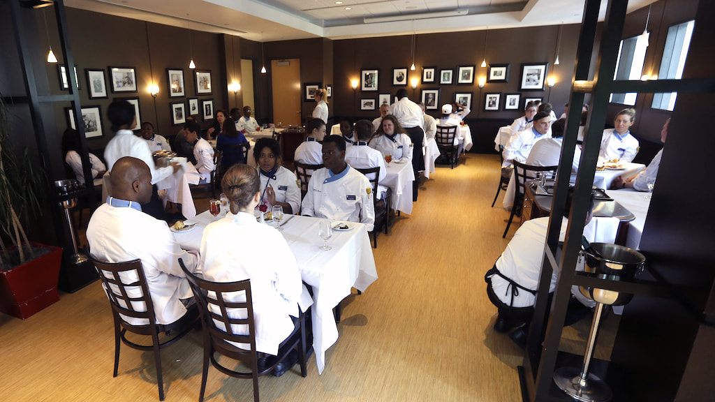Group of students at JWU Charlotte in a upscale dining area wearing chef uniforms 