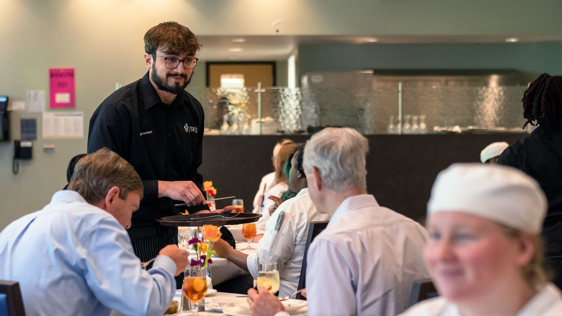 Male food and beverage industry management student at Charlotte JWU campus learn from hands on experience by serving a table of customers