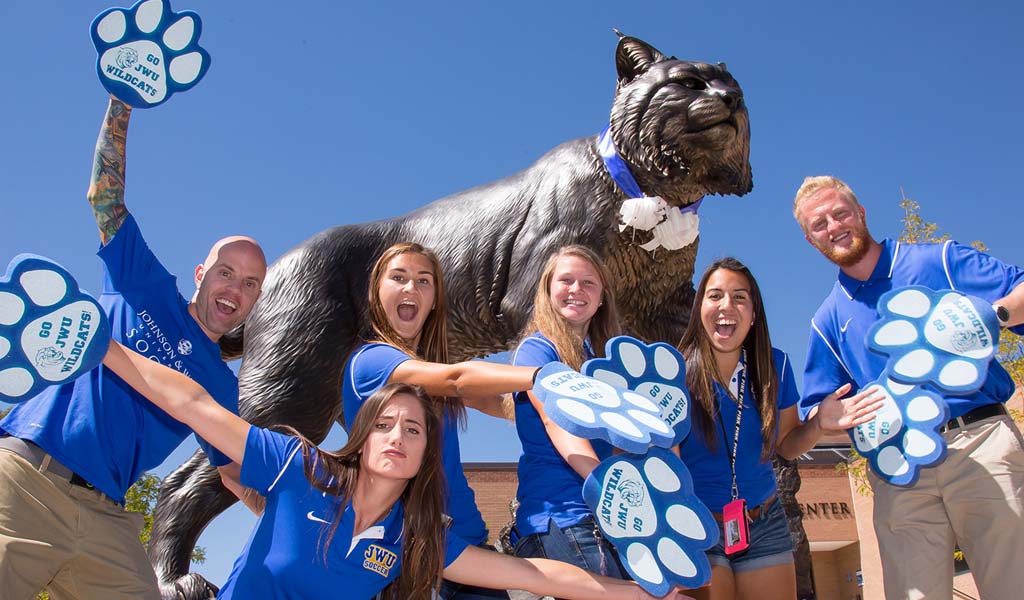 smiling students wearing paw foam hands in front of jwu wildcat statue