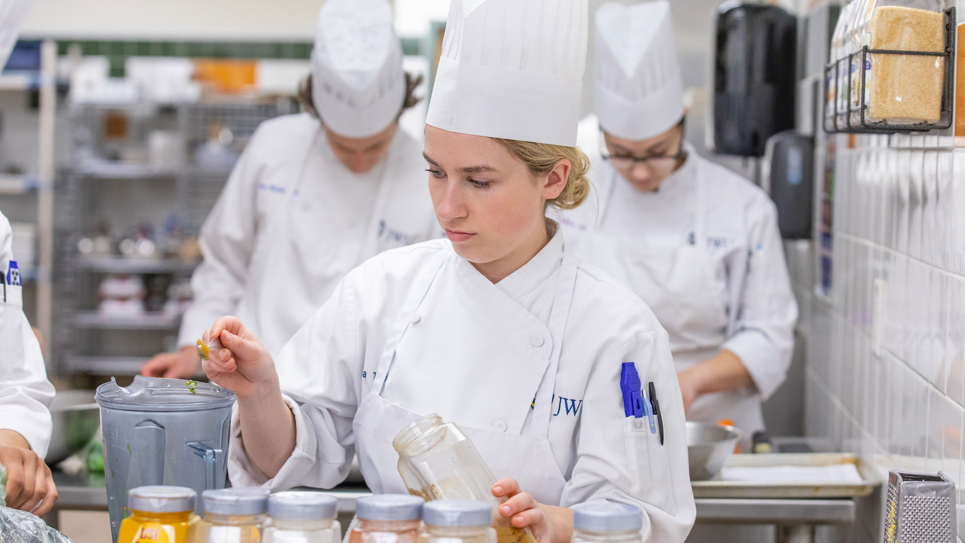 Culinary nutrition students in chef's uniforms cooking in campus kitchen