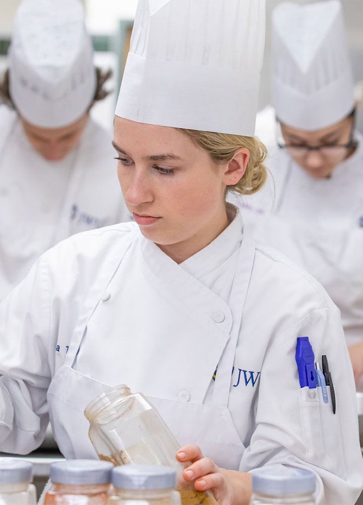 A culinary student working in a kitchen, holding a spice jar.