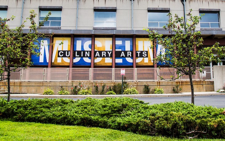 A modern building with a large "CULINARY ARTS MUSEUM" sign, surrounded by greenery under an overcast sky.