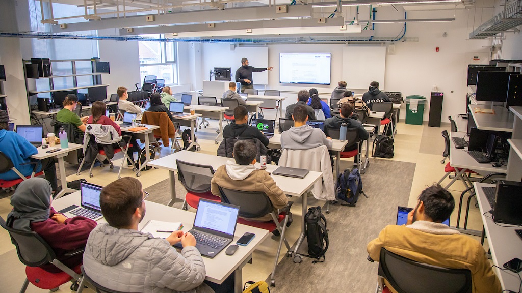 A person teaches a cybersecurity class to a group of students. 