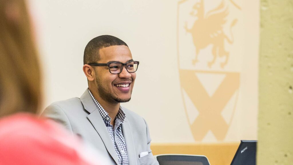 A professor teaching in a classroom, smiling at the students.