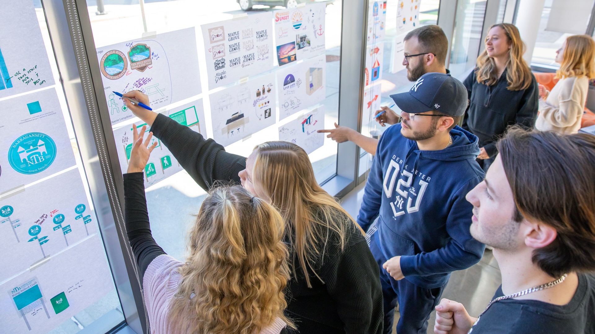 A group of students discuss design sketches posted on window