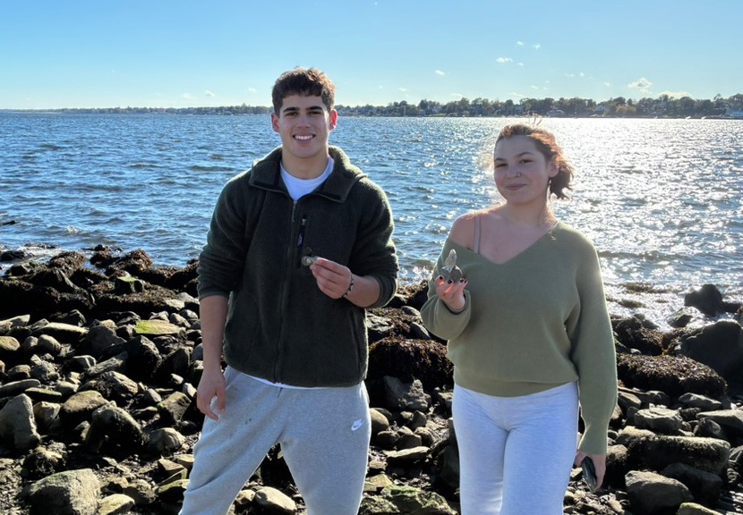 Two students on a reef in Narragansett Bay holding shells.