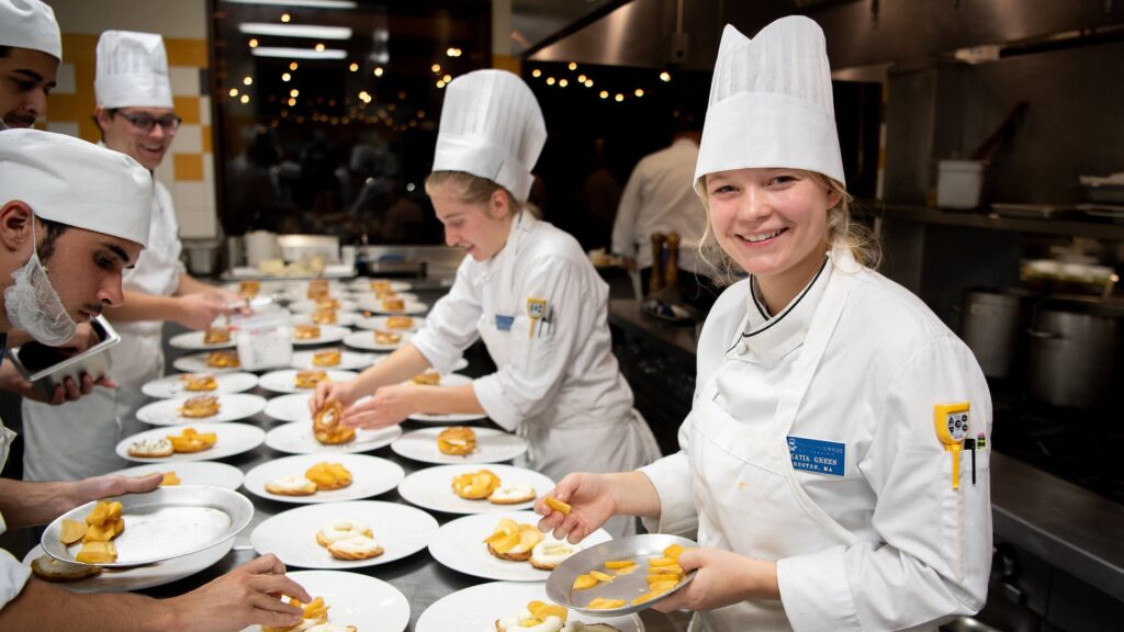 Culinary students smile as they prepare dishes for dinner service.