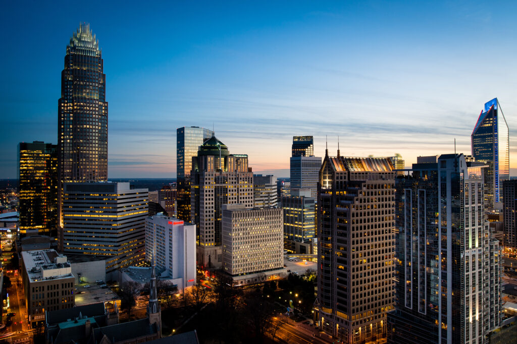 A city skyline at dusk, with illuminated skyscrapers against a gradient blue sky.