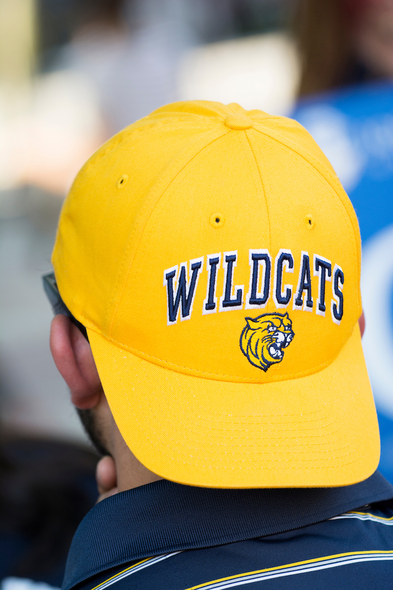 A person wears a bright yellow baseball cap with "WILDCATS" and a wildcat logo embroidered on the front.