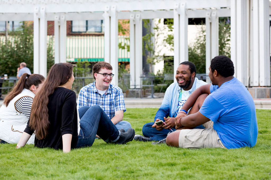 A group of students sitting on the grass, laughing and chatting together.
