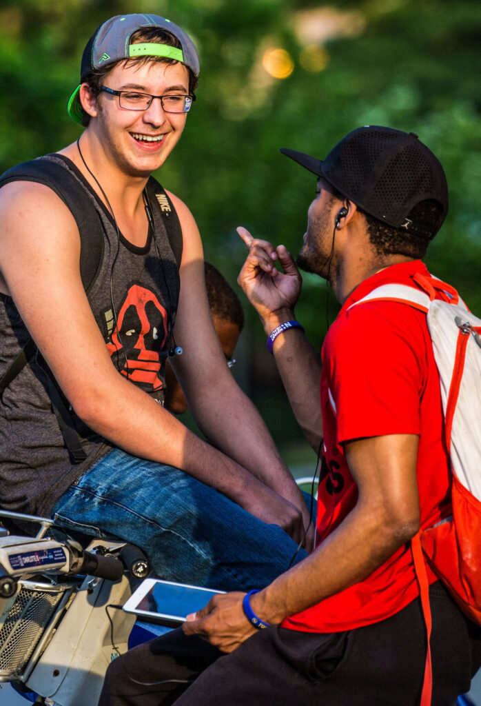 Three young people are laughing and talking together at a bike-sharing station near a Charlotte transit sign.