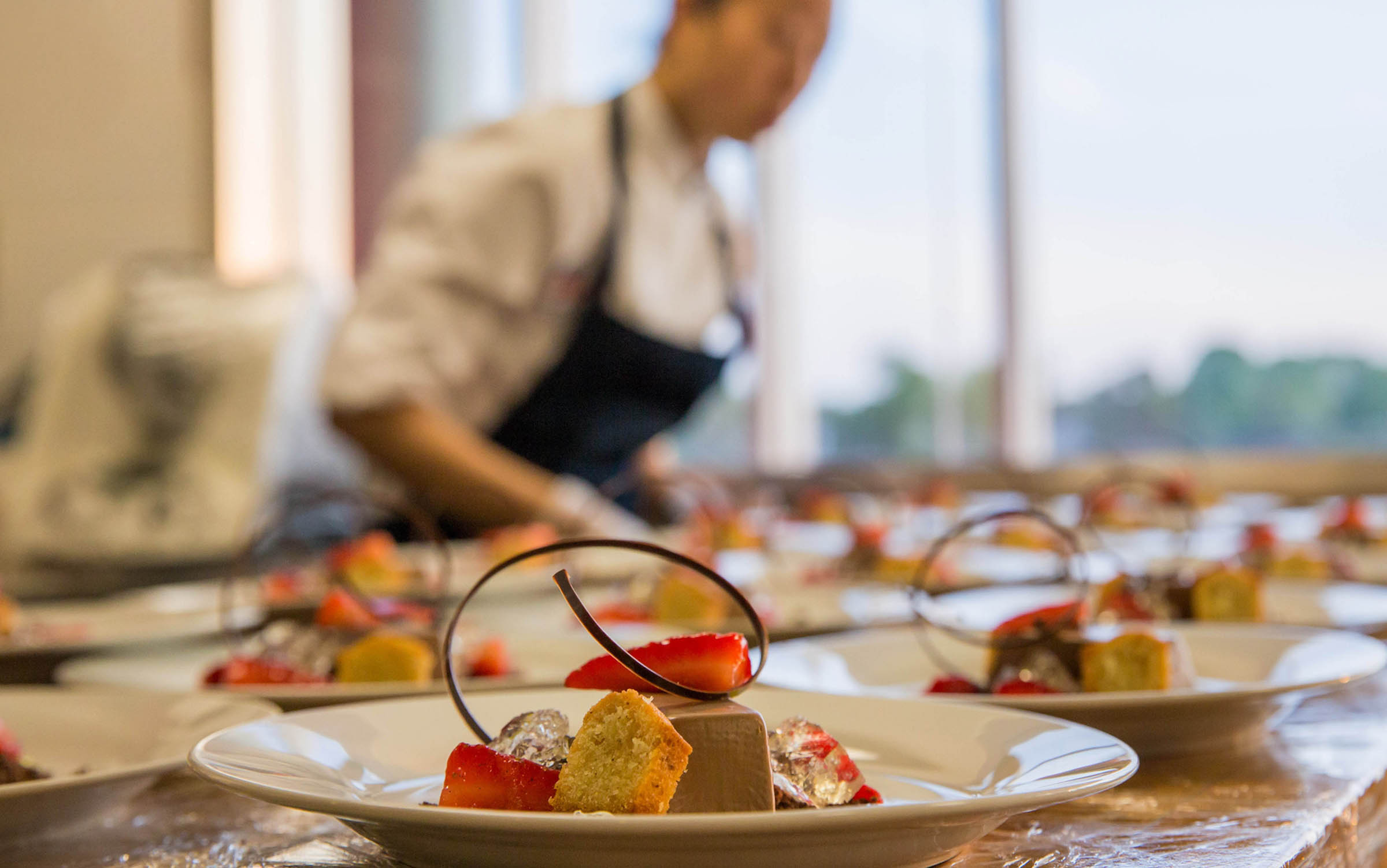 A chef prepares elegant dessert plates in a bright kitchen.
