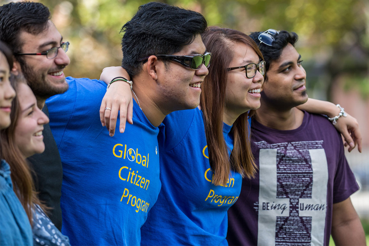 A group of individuals wearing "Global Citizen Program" shirts smile and stand together outdoors, arms around each other.