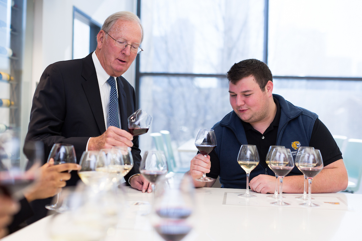 Two individuals engage in a wine tasting session, examining glasses of red and white wine at a table.