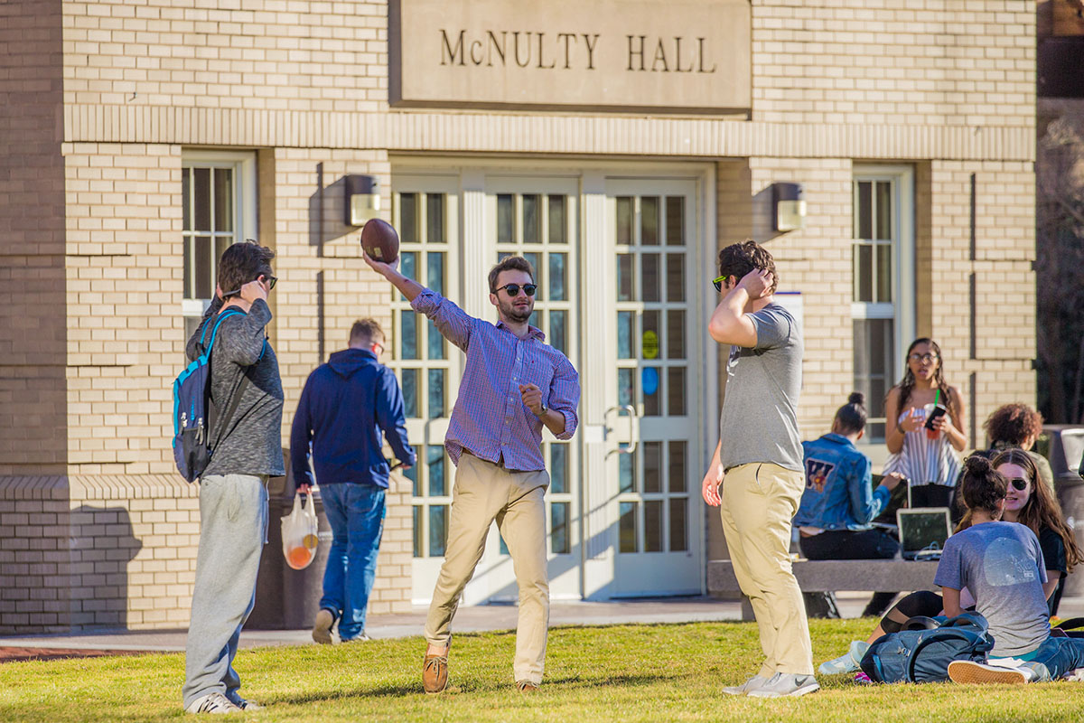 Students play catch with a football on a grassy area in front of McNulty Hall.