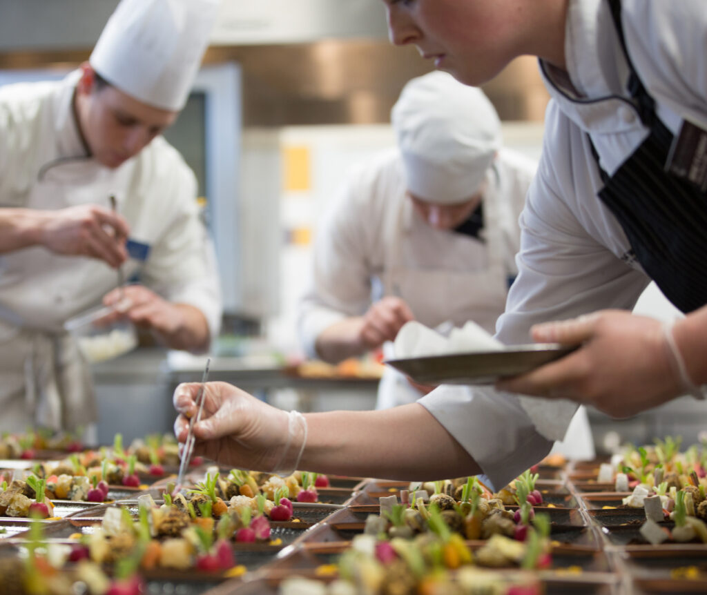 Chefs in a professional kitchen meticulously assemble small, colorful appetizers on trays.