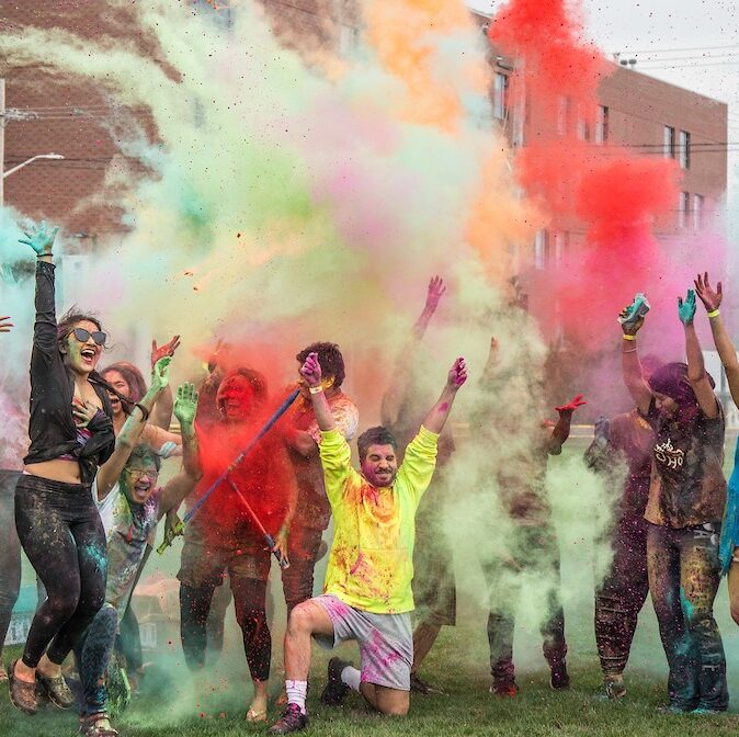 Students outside celebrating with colorful powder, throwing it up in the air.