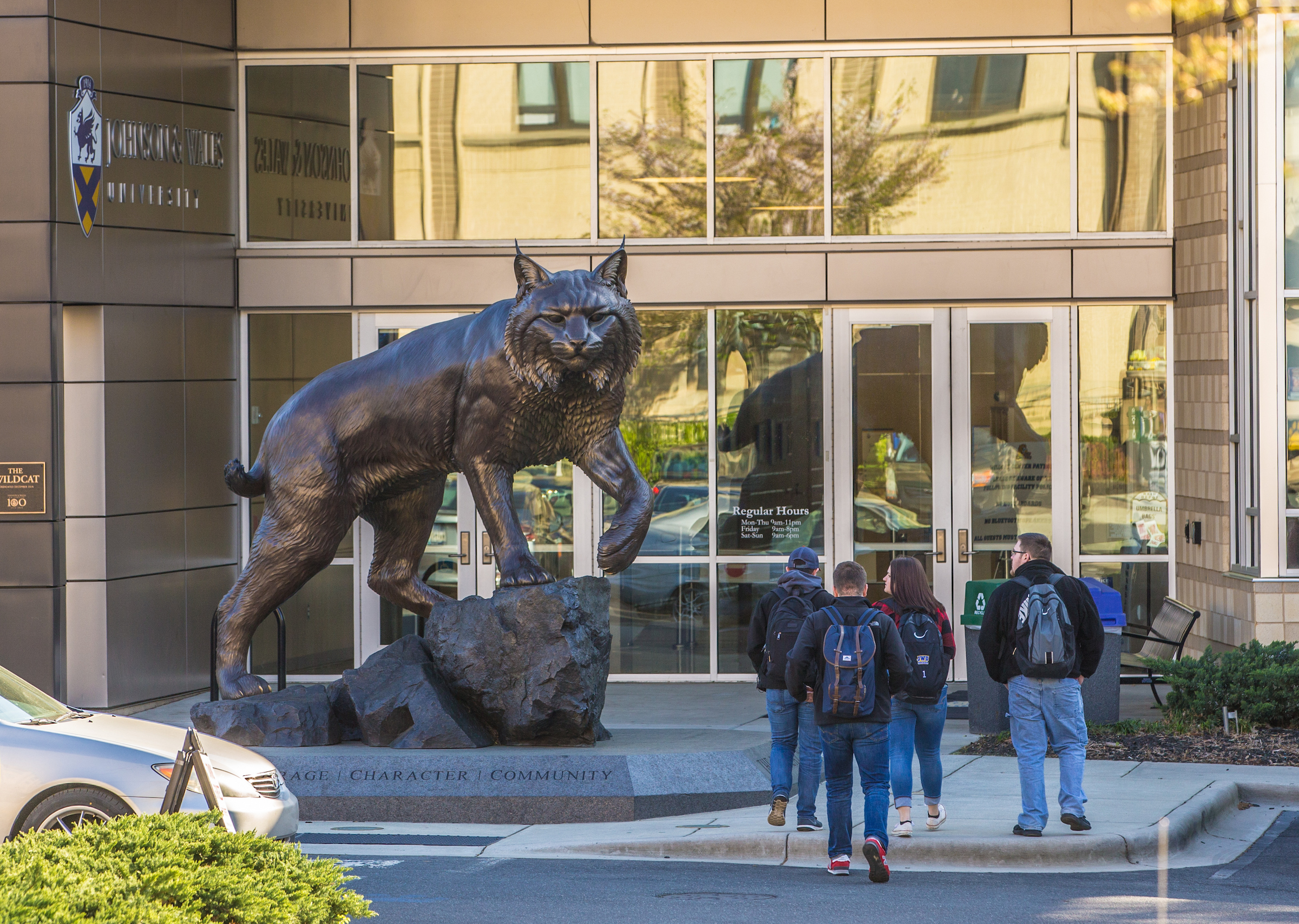 Students walk past a large bronze statue of a bobcat outside the entrance to Johnson & Wales University.