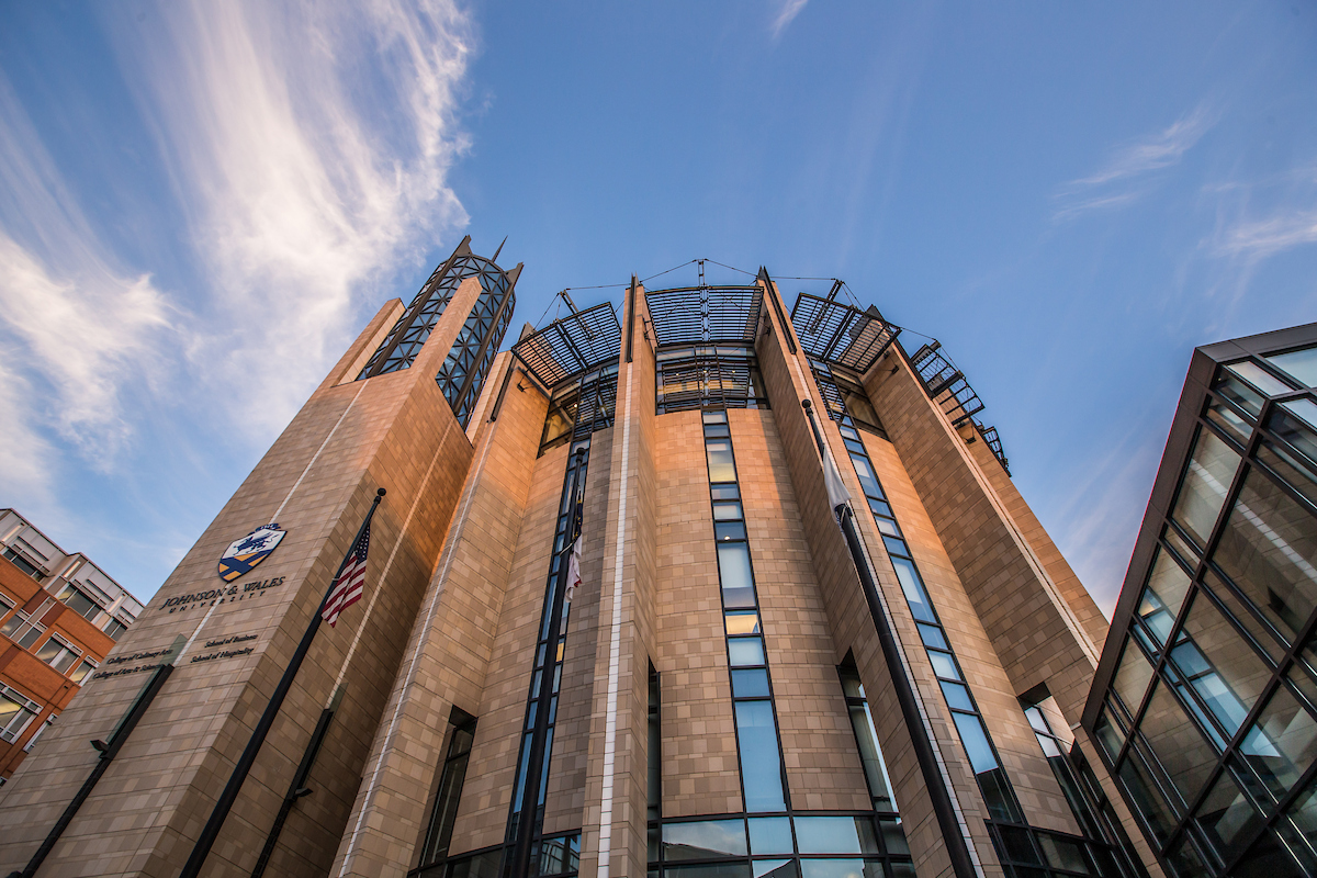 A modern university building with stone and glass architecture under a bright blue sky with wispy clouds.