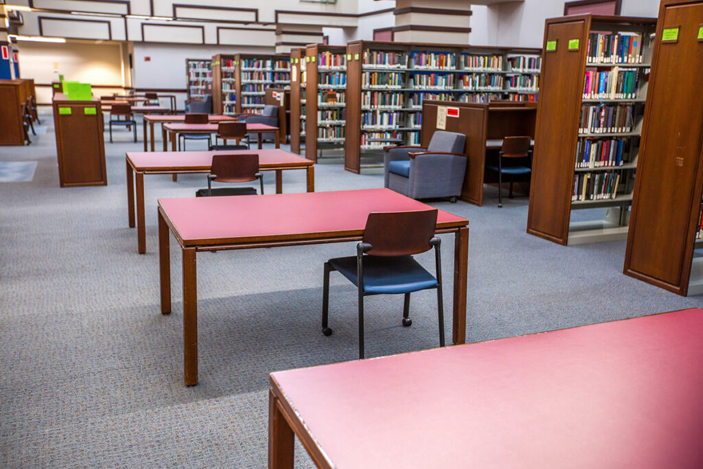 A view of the Providence library with rows of wooden tables, chairs, and bookshelves filled with books.