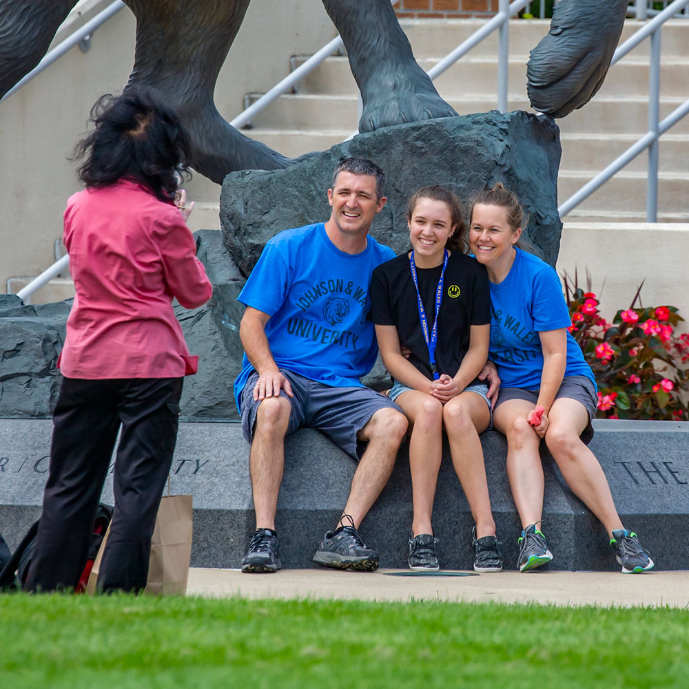 A family poses for a photo in front of the Wildcat statue on the Harborside campus.
