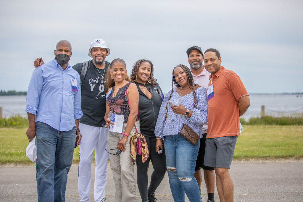 A group of seven people pose together outdoors near a body of water, smiling for the camera.