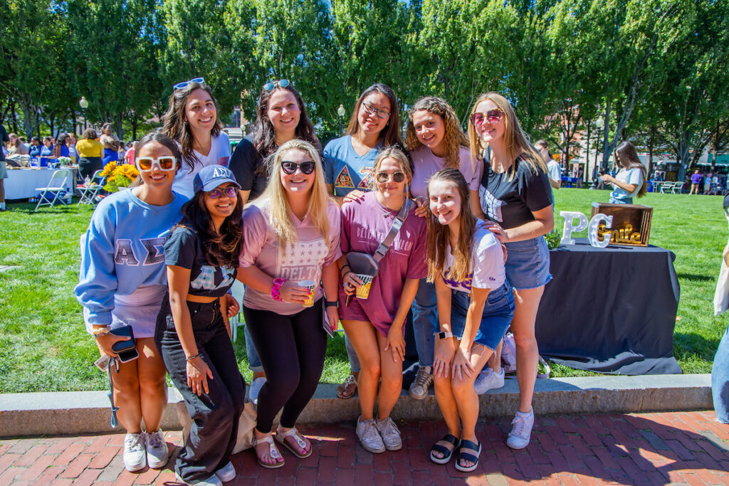 A group of young people in sorority apparel pose together outdoors on a sunny day.