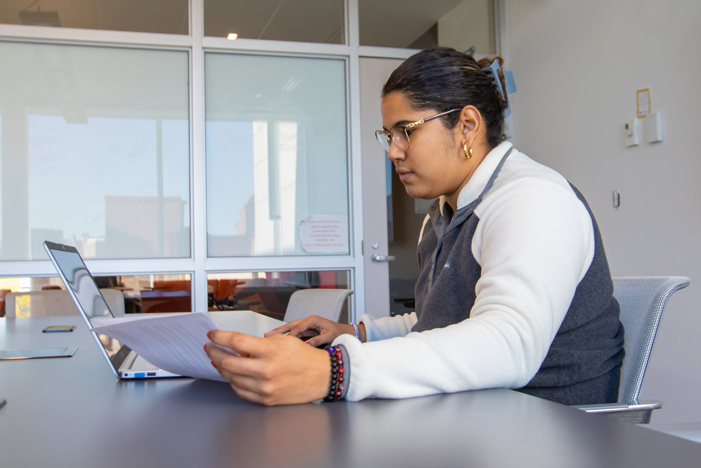 A student sits at a conference table, reviewing papers while using a laptop.