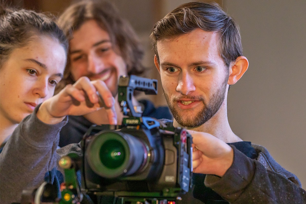 A group of students adjust a professional camera on a film set.