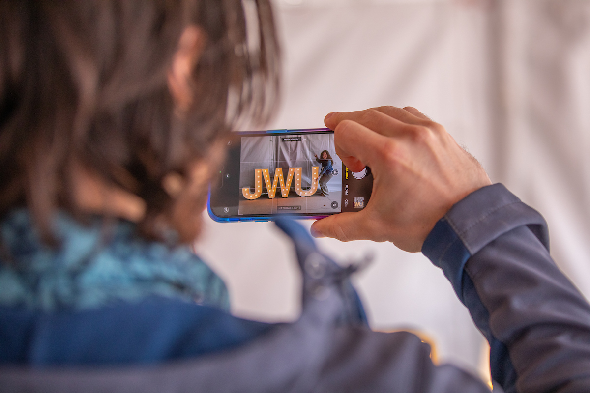 A person captures a photo of illuminated "JWU" letters on their smartphone.