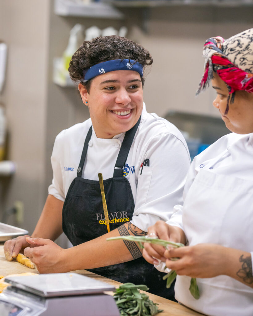 Two culinary students prepare ingredients together in a teaching kitchen.